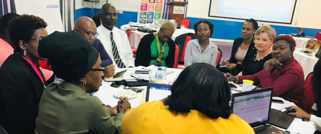 Members of the project team meet together at a table, discussing and taking notes on a laptop