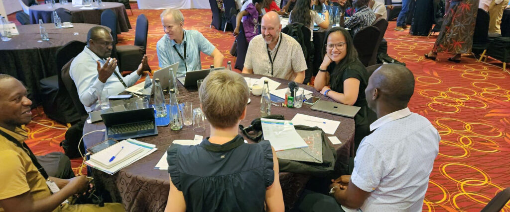 Diverse participants in the KBEST Institutional Partnership sit and work together around a large round table